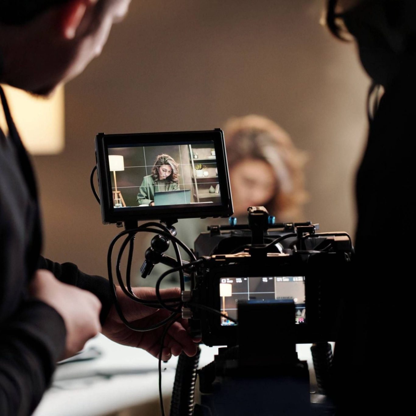 Une caméra filme une personne en arrière-plan, avec un écran de contrôle visible.