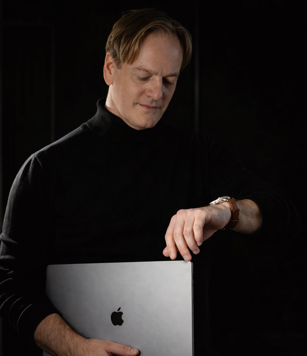 Olivier Dupont expert en vidéo LinkedIn et marque personnelle Homme en pull noir tenant un ordinateur portable Apple, regardant sa montre.