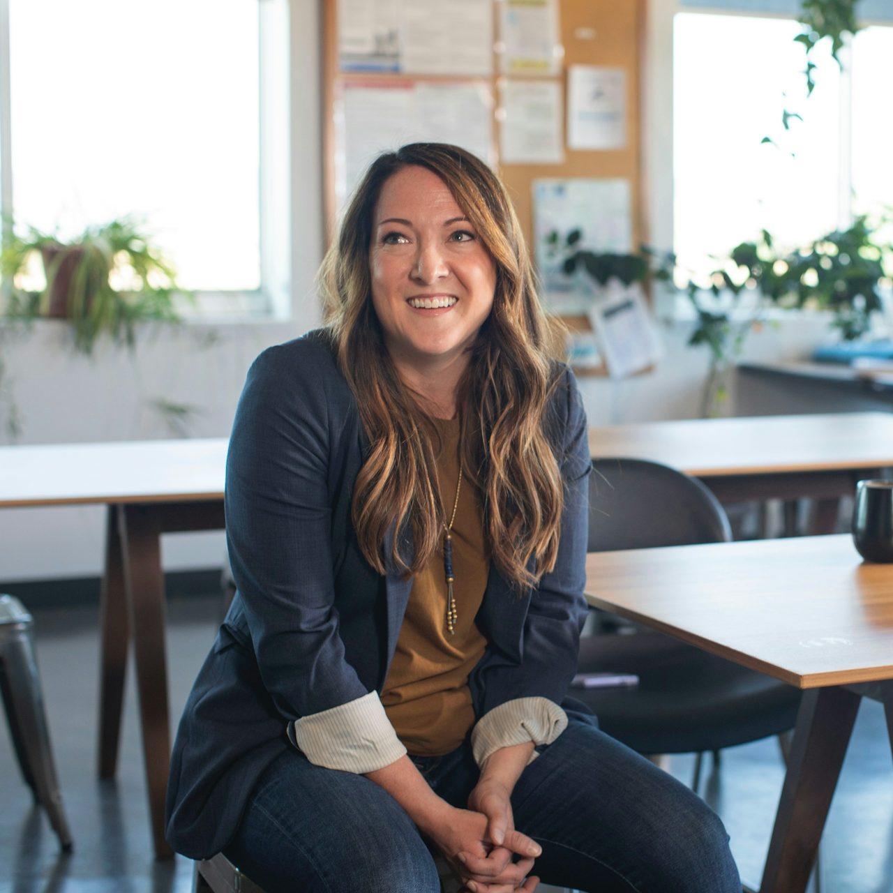 Coach, consultant et expert Femme souriante assise, vêtue d'une veste, dans un bureau lumineux avec des plantes.
